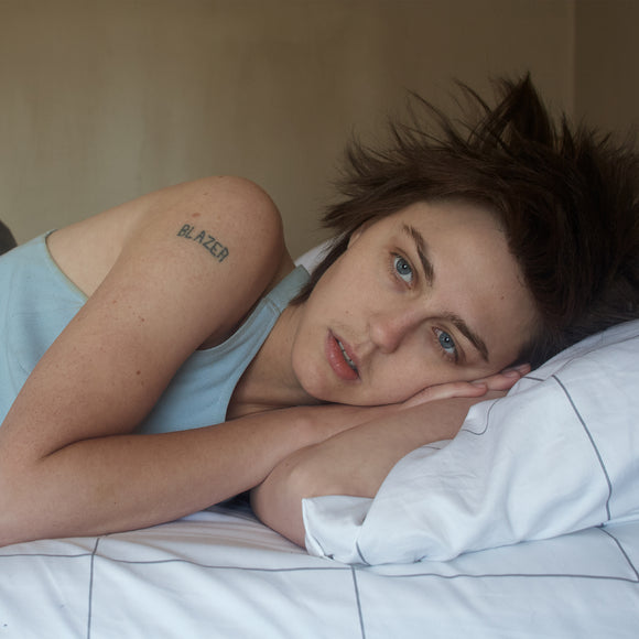 I Saw First Light by Anna McClellan on Father/Daughter Records (the album cover is a full-sleeve colour medium close-up photograph of Anna McClellan lying on a bed; McClellan wears a vest and has bed-head hair; on their bare right shoulder is a tattoo of the word 'BLAZER'