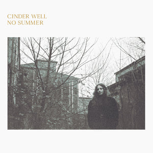 No Summer by Cinder Well on Free Dirt Records (the album cover features a black and white rectangular photograph of Amelia Baker stood in front of leafless trees and stone buildings beneath a white sky; the photgraph is on a plain white background, and the artist name and album title are printed in a n uppercase light gold serif font at the top-left of the sleeve)