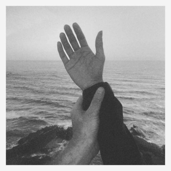 Unbecoming by Eli Winter on American Dreams Records (the album cover is a balck and white photograph of a hand being raised against the backdrop of an open sea, palm open and held at the wrist by another hand; there is no text or information on the front cover; the photograph is surrounded by the narrow white border).