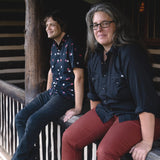 Colour photograph by Eli Johnson of William Tyler and Marisa Anderson sat on the porch of a log cabin