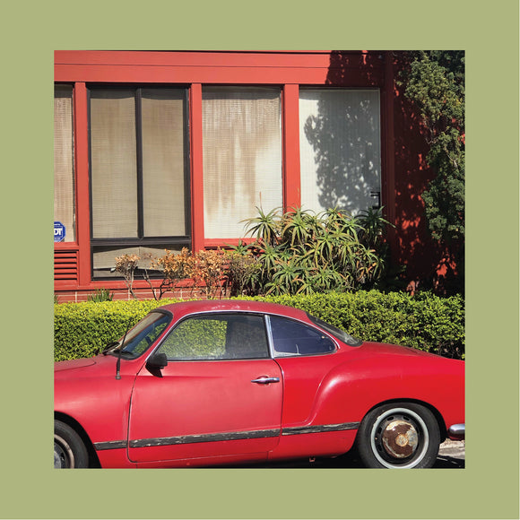 The Town That Cursed Your Name by The Reds, Pinks & Purples on Tough Love Records (the album artwork features a square colour photograph of an old red car sports car parked outside of a red suburban house with a hedge and shrubs in the garden; the photograph is bordered with pastel-olive green on all sides; there is no text or other information on the front of the sleeve)
